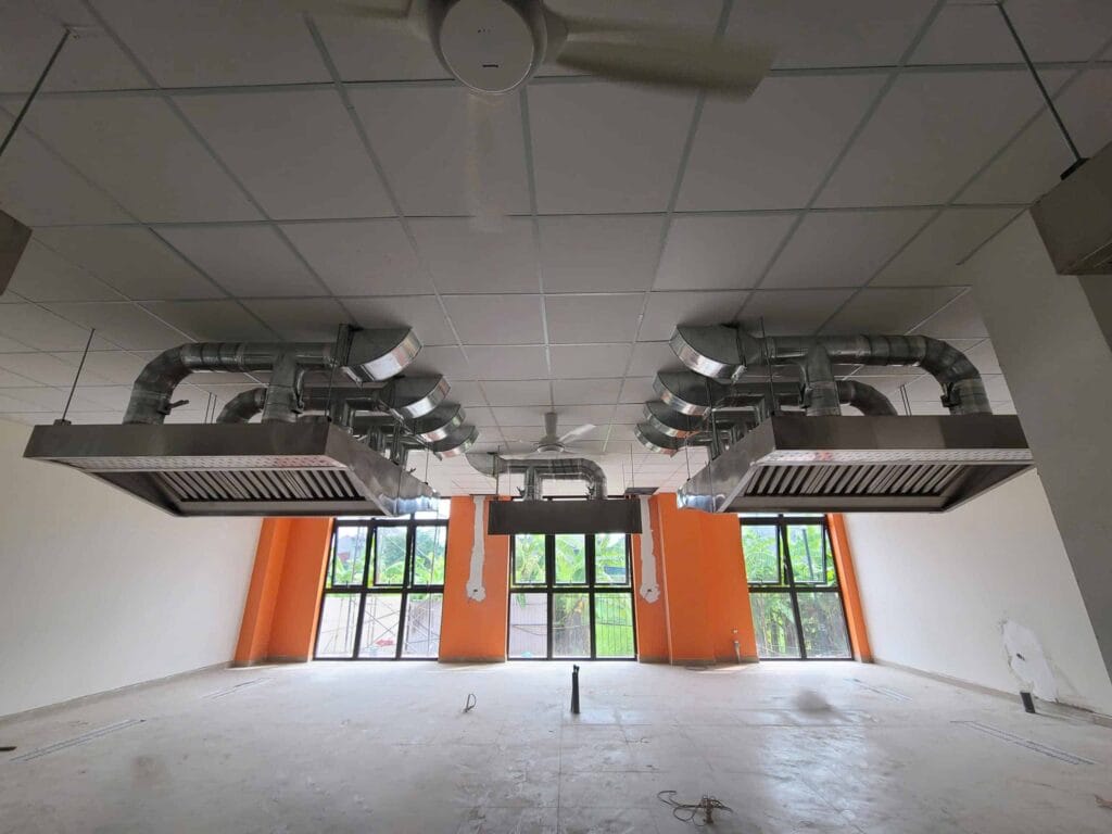 Góc nhìn toàn cảnh hệ thống hút mùi và thông gió công nghiệp với hai máng hút khói lớn bằng inox sáng bóng, kết nối với ống dẫn khí trên trần thạch cao của khu vực bếp nhà hàng/bếp thương mại đang hoàn thiện.